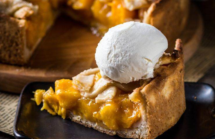 una fetta di crostata alle pesche con pallina di gelato